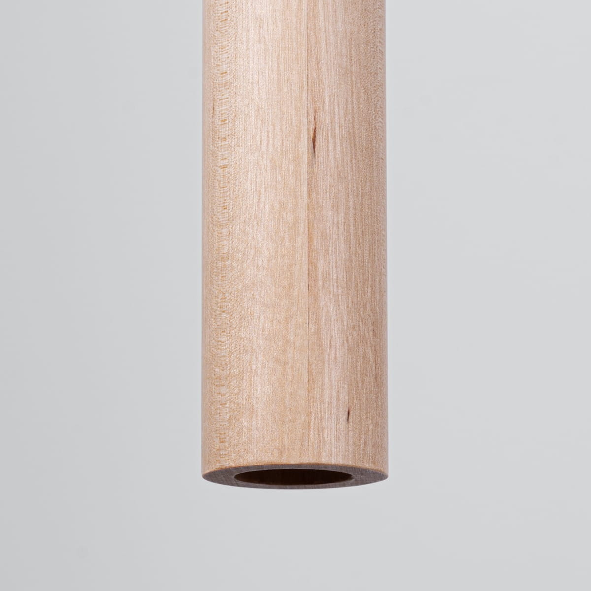 Lampa wisząca Pastelo z oprawą w kolorze czarnym i drewnianym elementem w naturalnym odcieniu. Widoczny detal drewnianej rurki z otworem, zawieszony w pionie na jednolitym tle.