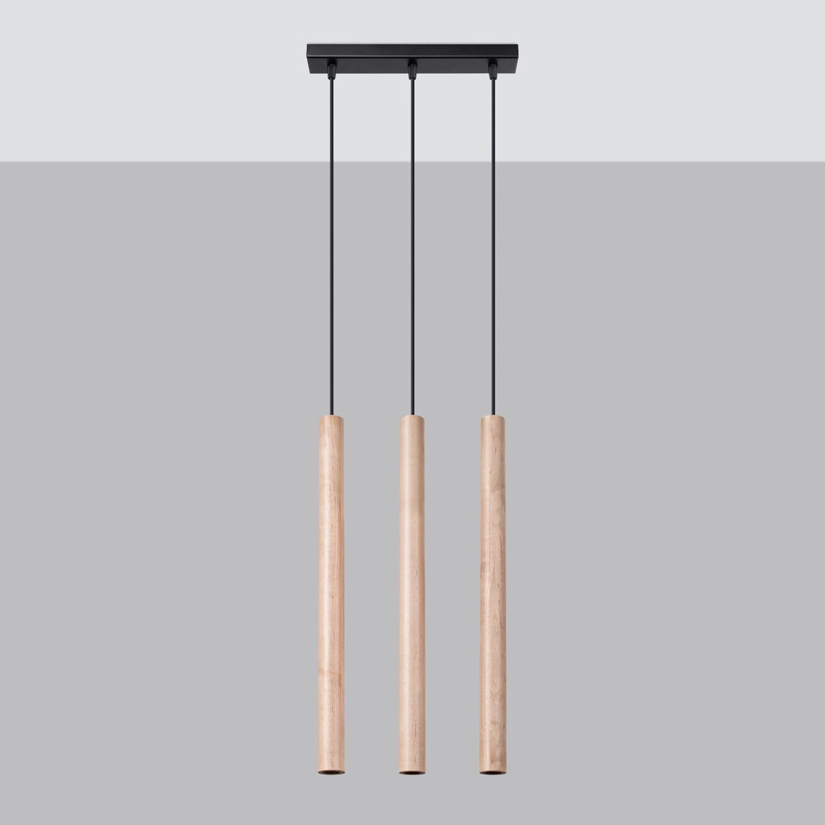 Lampa wisząca Pastelo z trzema cylindrycznymi kloszami w kolorze naturalnego drewna, zawieszona na czarnych zwisach, zamocowana do prostokątnej czarnej podstawy. Produkt ma nowoczesny design, idealny do różnych aranżacji wnętrz.