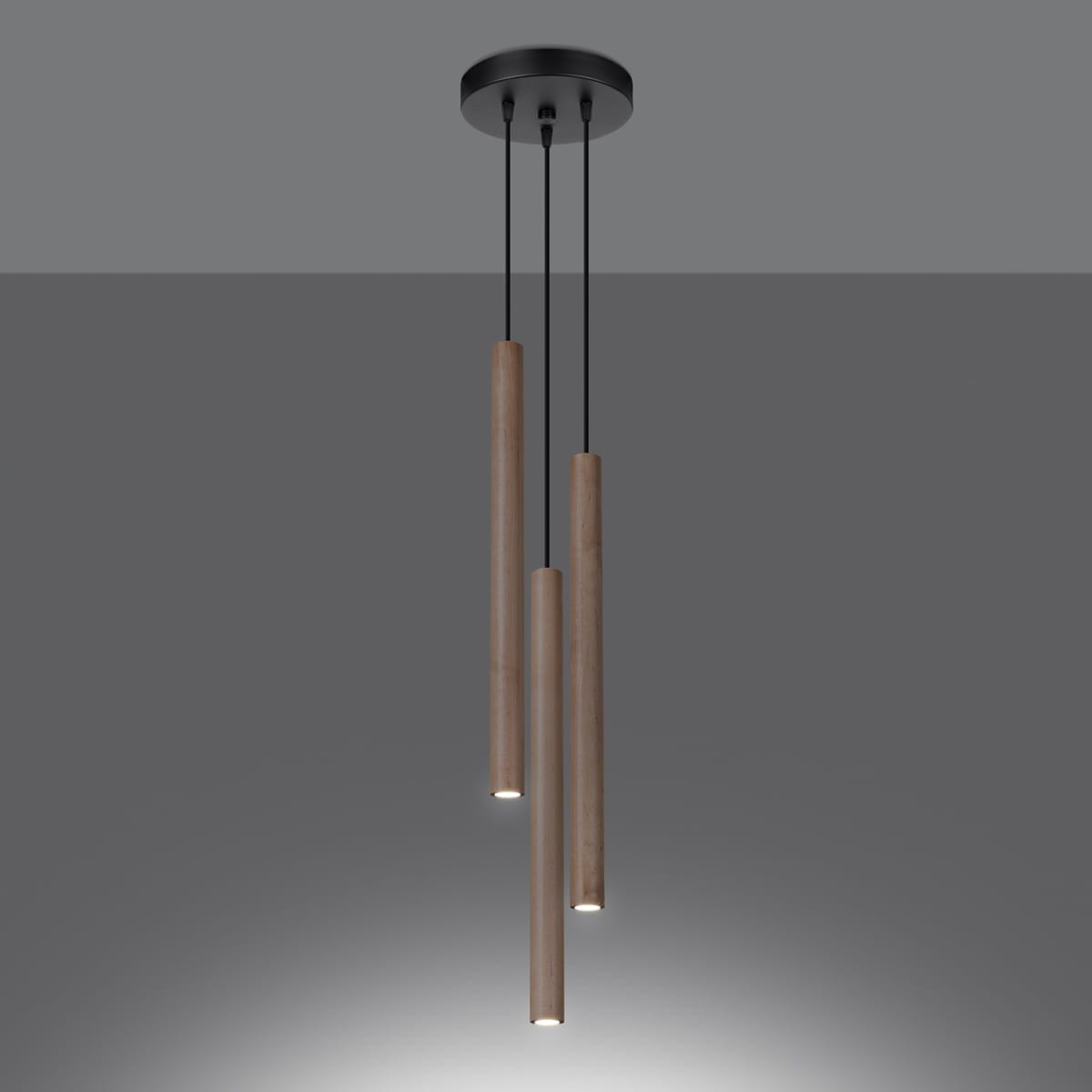 Lampa wisząca Pastelo w kolorze czarnym z drewnianymi elementami, składająca się z trzech cylindrycznych opraw, zawieszonych na czarnych przewodach. Ujęcie z góry, z widocznymi źródłami światła na dole każdego elementu.