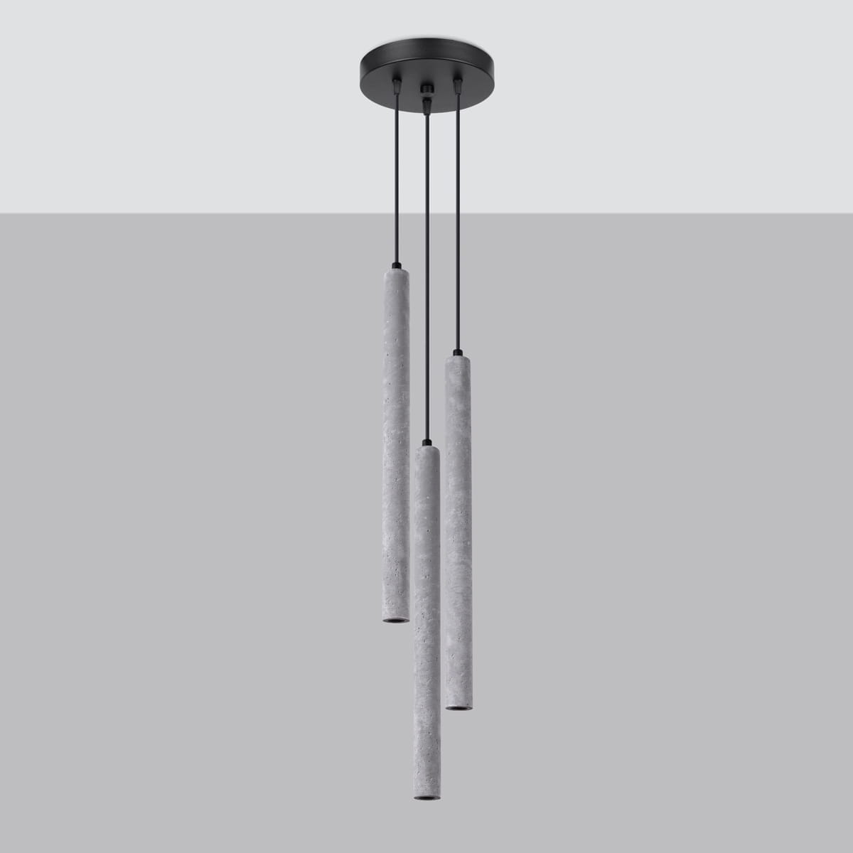 Lampa wisząca Pastelo z trzema cylindrycznymi kloszami w kolorze betonu, zawieszona na czarnych kablach. Klosze mają matową teksturę, a całość montowana jest do okrągłej czarnej podstawy sufitowej. Tło w jasnoszarym odcieniu.