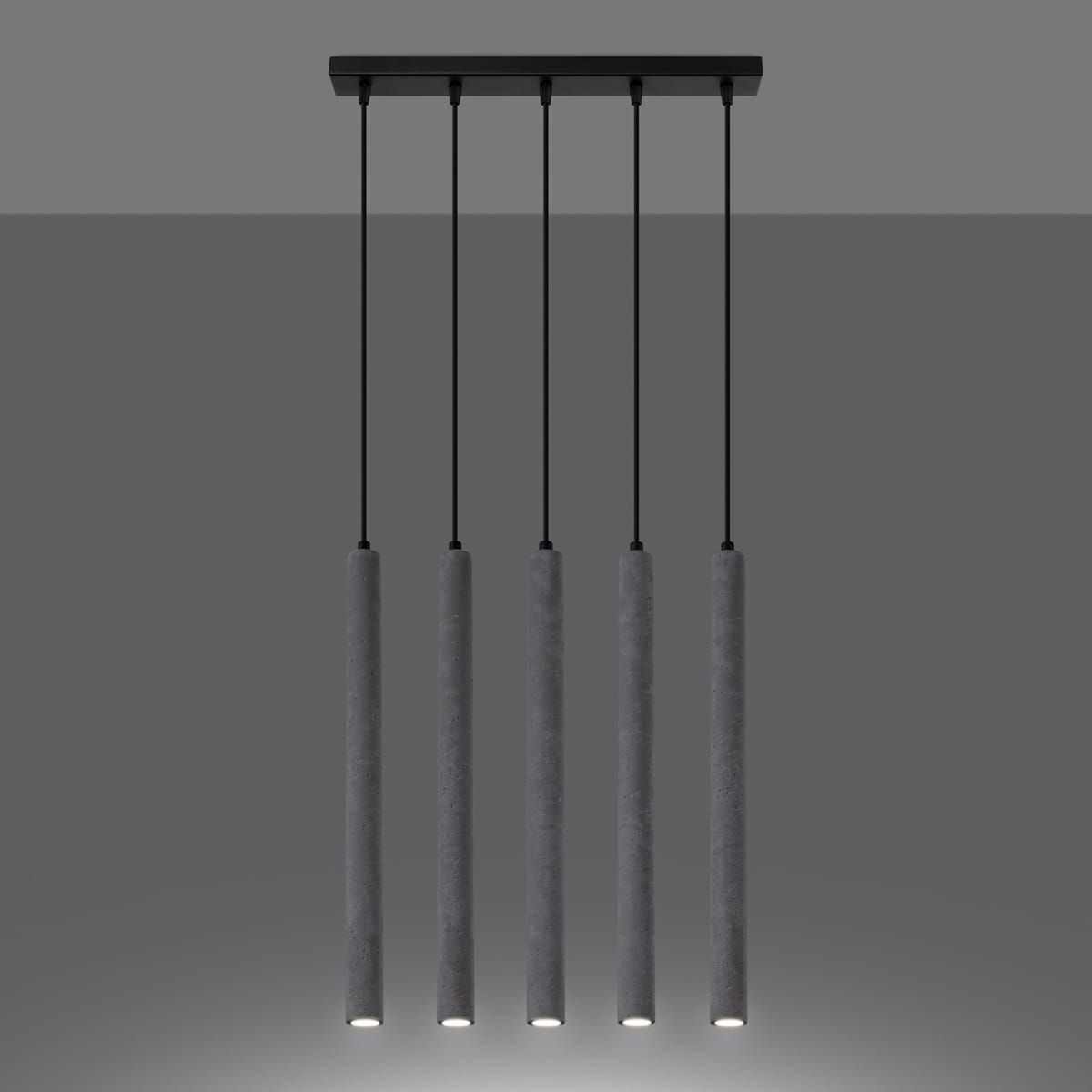 Lampa wisząca Pastelo w kolorze czarnym i betonowym, składająca się z pięciu cylindrycznych źródeł światła na długich, cienkich przewodach. Produkt zawieszony na prostokątnej podstawie, z widocznymi diodami LED na dole każdego cylindra.