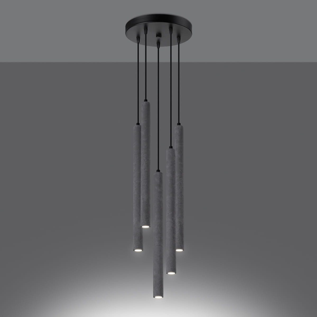 Lampa wisząca Pastelo w kolorze czarnym z pięcioma cylindrycznymi kloszami z betonu, zawieszona na cienkich czarnych przewodach. Klosze mają zamontowane źródła światła na dole. Lampa ma okrągłą podstawę mocującą.