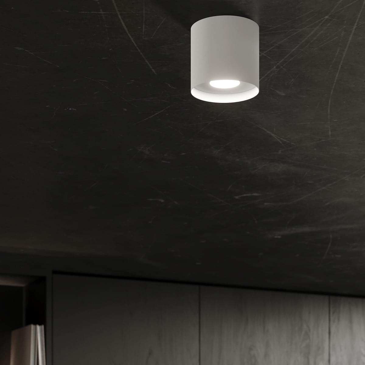 Lampa sufitowa Mika w kolorze białym z miejscem na jedną żarówkę GU10. Zamontowana na ciemnym suficie, o cylindrycznym kształcie z delikatnym wykończeniem, emituje jasne światło, dodając nowoczesnego stylu wnętrzu.