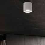 Lampa sufitowa Mika w kolorze białym z miejscem na jedną żarówkę GU10. Zamontowana na ciemnym suficie, o cylindrycznym kształcie z delikatnym wykończeniem, emituje jasne światło, dodając nowoczesnego stylu wnętrzu.