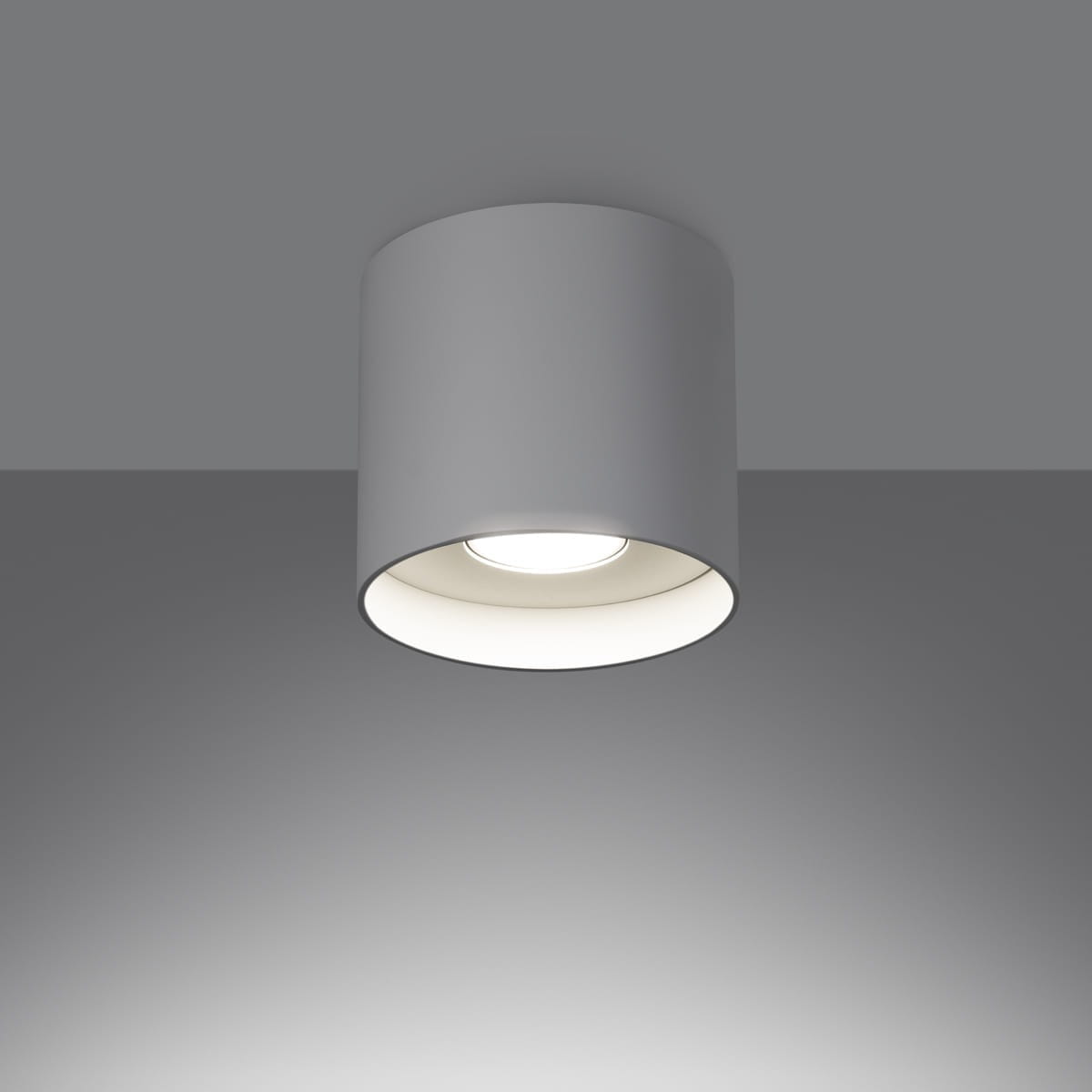 Biała lampa sufitowa Mika z jedną oprawą GU10, o cylindrycznym kształcie, montowana na suficie. Widoczny jasny klosz wewnętrzny i minimalistyczny design. Lampa o prostym wyglądzie, umieszczona na jednolitym tle.