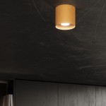 Lampa sufitowa Mika w kolorze złotym, okrągła, zamontowana na ciemnym suficie. Posiada źródło światła GU10, emitujące jasne światło. Widok z dołu, ukazujący prosty design i gładką powierzchnię.