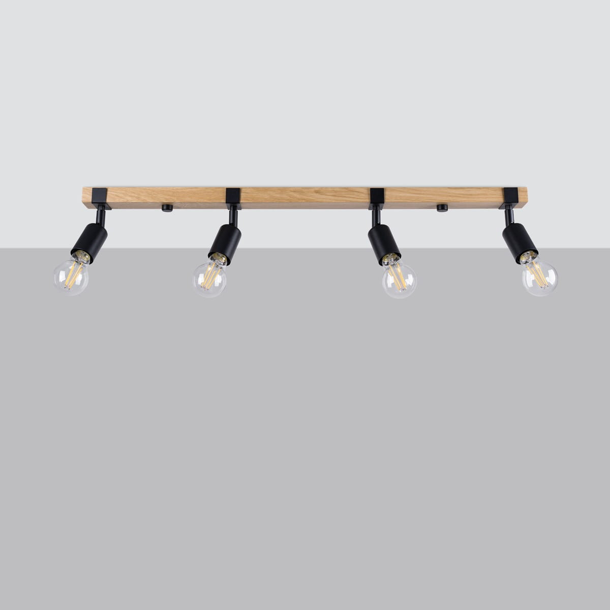 Lampa sufitowa Zuca, czarna z jasnym drewnem, z trzema reflektorami na regulowanych ramionach, zamontowana na drewnianej listwie. Prosta konstrukcja, idealna do nowoczesnych wnętrz. W tle jednolite, jasne.