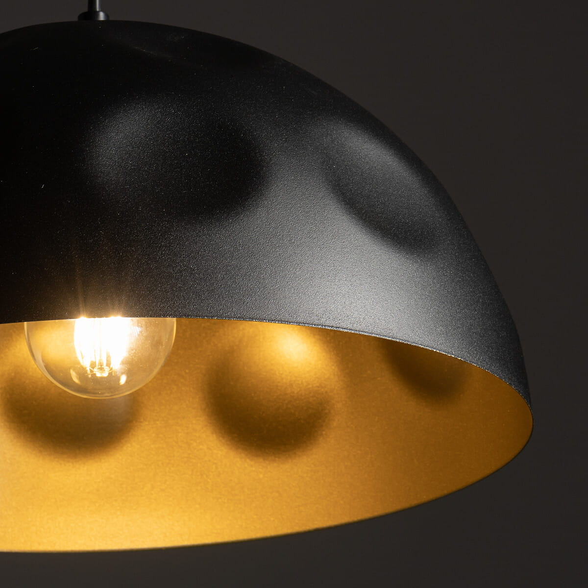 Lampa wisząca Hemisphere Hit D50 z kloszem w kolorze czarnym z złotym wykończeniem. Widoczna żarówka E27 w przezroczystym kloszu. Klosz ma zaokrąglony kształt z teksturą na zewnętrznej stronie, zwisający z cienkiego przewodu.