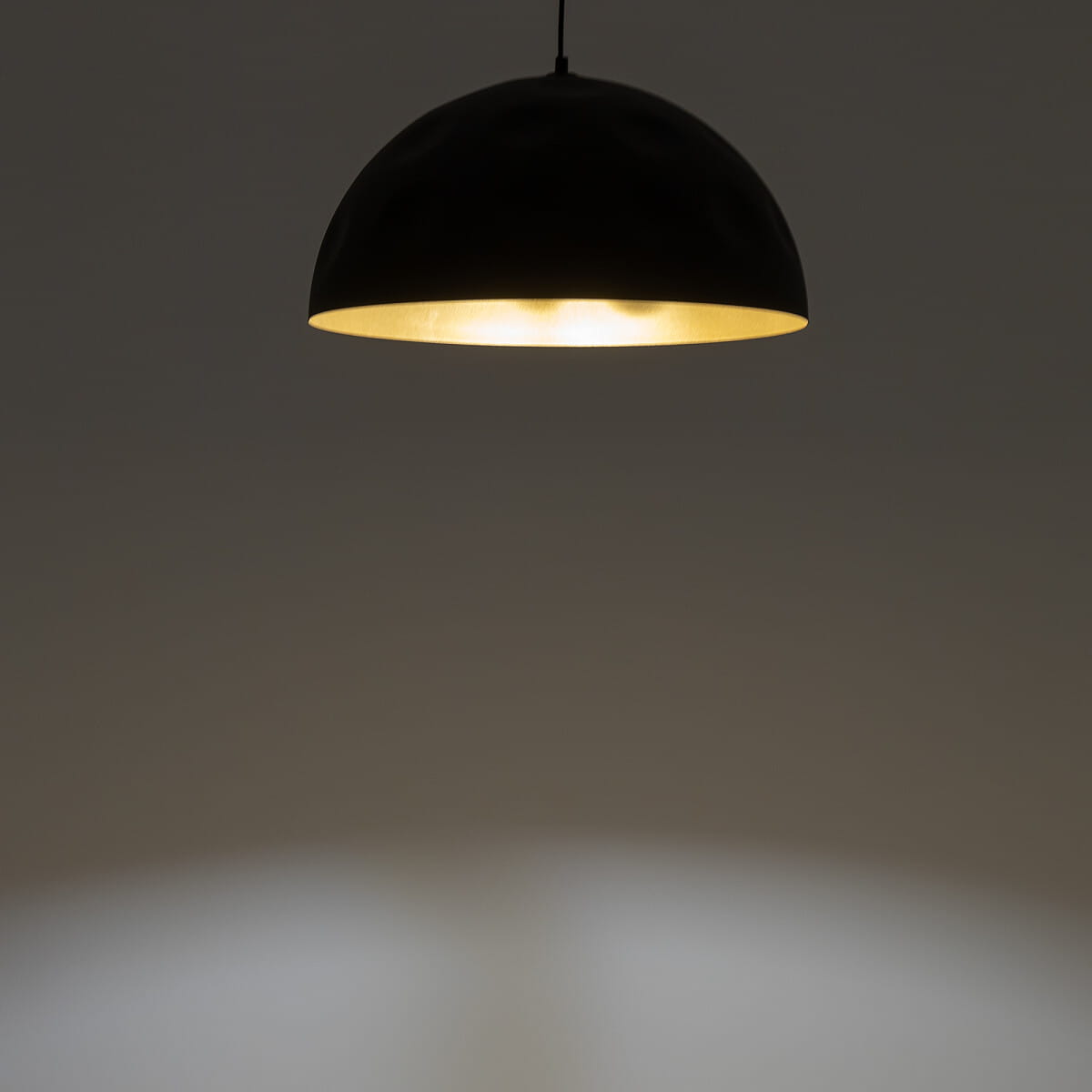 Lampa wisząca Hemisphere Hit D50 w kolorze czarnym z wewnętrzną złotą powłoką, zawieszona na cienkim kabelku. Kształt półkolisty, emitująca ciepłe światło, umieszczona w minimalistycznym otoczeniu.