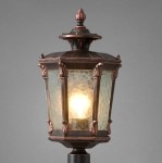 Lampa stojąca ogrodowa Amur 1-punktowa, w kształcie latarni. Metalowa obudowa w kolorze mosiężnym z dekoracyjnymi detalami, szklane ścianki w stylu witrażowym. Źródło światła widoczne w środku, całość na ciemnym tle.