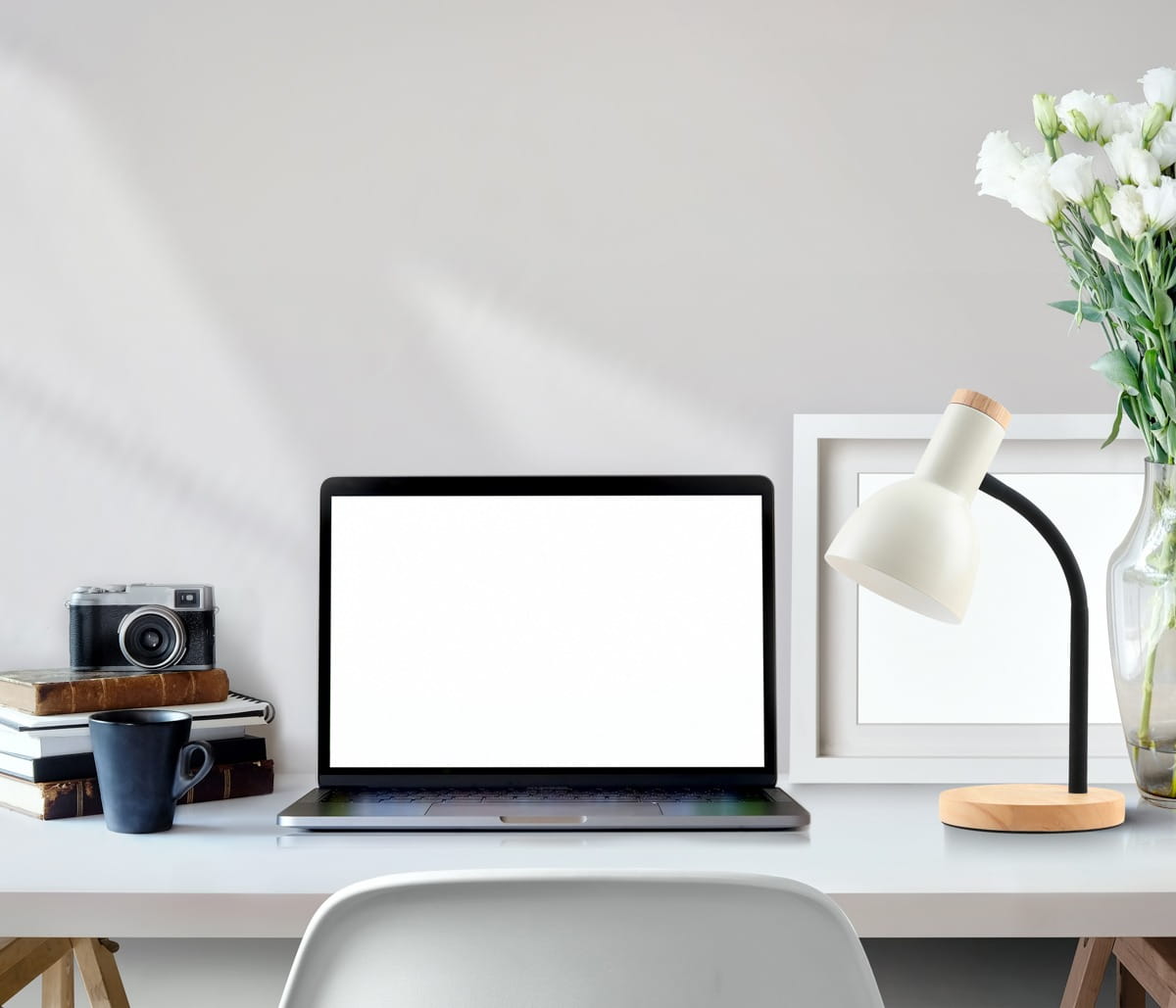 Lampka biurkowa Senza w kolorze białym, z metalowym kloszem i drewnianą podstawą. Ustawiona obok laptopa na biurku, w otoczeniu książek, kubka i kwiatu w wazonie. Kąt ujęcia z boku, ukazujący detale lampki oraz aranżację biura.