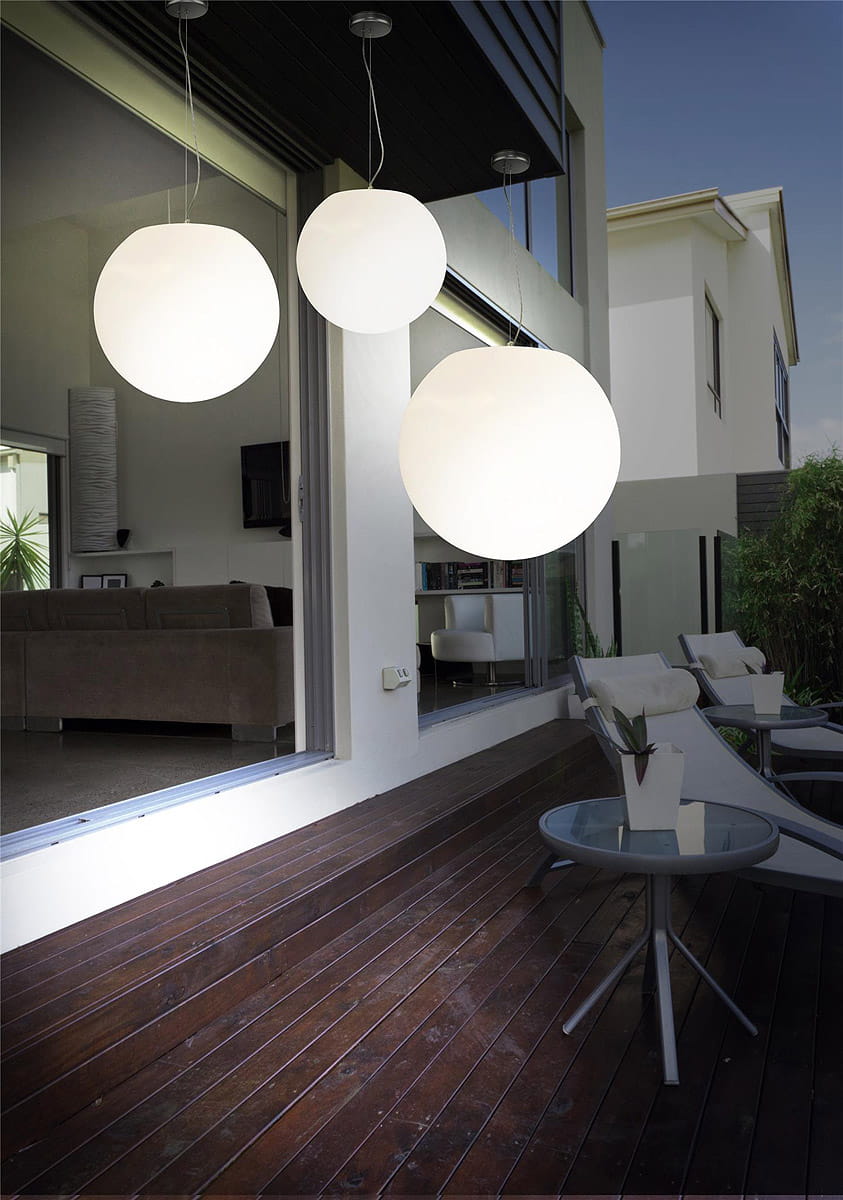 Lampa ogrodowa wisząca Cumulus S w kształcie białych, okrągłych kul, zawieszona pod sufitem nad drewnianym tarasem. W tle widoczny nowoczesny salon z szarym sofą i dużymi oknami, otoczenie zieleni.
