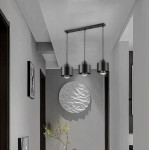 Lampa wisząca Elza z trzema gniazdami E27, w kolorze czarnym, zawieszona na prostokątnej podstawie. Lampy mają cylindryczny kształt i są zamontowane na równych długościach, w nowoczesnym wnętrzu z szarymi ścianami.