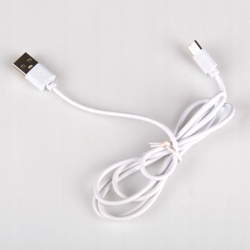 Biała lampka biurkowa Alma LED 12W z funkcją CCT i RGB. Widoczny kabel USB, umożliwiający zasilanie, w kolorze białym. Produkt leży na jasnym tle, z wyraźnym widokiem na złącze USB i przewód.