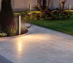 Lampa stojąca ogrodowa Grado 3K w kolorze czarnym, wysokość 70 cm, z jedną diodą LED 12W, 3000K, umieszczona na ścieżce w ogrodzie, otoczona roślinnością i kwiatami, oświetlająca teren w dolnej części, z prostym, cylindrycznym kształtem.