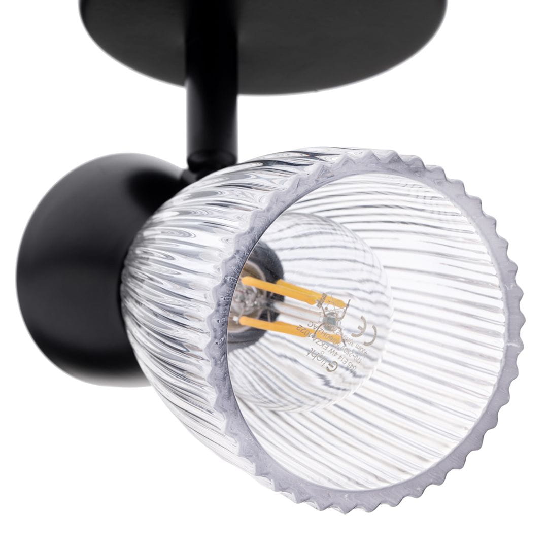 Lampa sufitowa typu spot w kolorze czarnym z jedną oprawą na żarówkę E14. Szklany klosz o fakturze w pionowe prążki, zamontowany na okrągłej podstawie. Ujęcie z boku, ukazujące szczegóły klosza oraz miejsce na żarówkę.