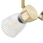 Złota lampa sufitowa typu spot z dwoma oprawami na żarówki E14. Przezroczysta klosz z rowkowaną fakturą, zamocowany na okrągłej, matowej podstawie. Ujęcie z boku, podkreślające detale konstrukcji.
