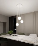Lampa wisząca Royal 3-punktowa w kolorze białym i złotym, z trzema okrągłymi kloszami, zawieszona na długich przewodach. Widoczna w aranżacji nad stołem z marmurowym blatem oraz zielonymi krzesłami w nowoczesnym wnętrzu.