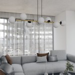 Lampa wisząca Gravity 8-punktowa w kolorze czarnym i złotym, z białymi kulami, umieszczona nad szarym narożnikiem. Wisi na dwóch czarnych linkach, w nowoczesnym wnętrzu z dużymi oknami i zasłonami.