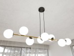 Lampa wisząca Gravity 8-punktowa, czarna i złota. Konstrukcja z metalowego stelaża z ośmioma okrągłymi kloszami opalowymi. Ujęcie z dołu, pokazujące lampę zawieszoną na czarnych przewodach w jasnym wnętrzu z oknem i zasłonami.