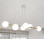Lampa wisząca Gravity 6-punktowa w kolorze białym i złotym. Składa się z sześciu opalowych kul na złotej rurze, zawieszona na dwóch białych linkach. Ujęcie z góry, w jasnym wnętrzu z zasłonami w tle.