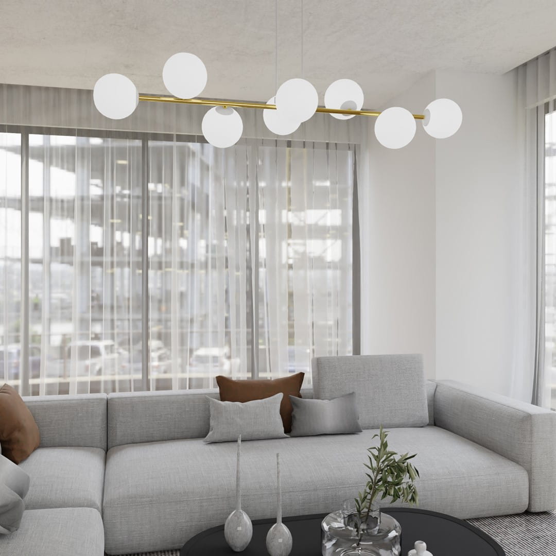 Lampa wisząca Gravity 8-punktowa w białym i złotym kolorze z opalowymi kloszami, umieszczona nad szarym narożnikiem. Klosze mają okrągły kształt, a lampa jest zawieszona na złotej rurze, tworząc nowoczesny element w aranżacji wnętrza.