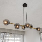 Lampa wisząca Gravity 6-punktowa w kolorze czarnym, złotym i grafitowym. Składa się z sześciu szklanych kul o metalicznym wykończeniu, zawieszonych na złotej rurze. Ujęcie z góry, na tle jasnego sufitu i zasłon.
