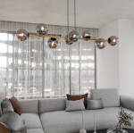 Lampa wisząca Gravity 8-punktowa w kolorze czarnym, złotym i grafitowym. Posiada osiem okrągłych, metalicznych kloszy na cienkiej, złotej listwie. Zawieszona na dwóch czarnych linkach, umiejscowiona nad szaro-beżową sofą we wnętrzu z dużymi oknami.