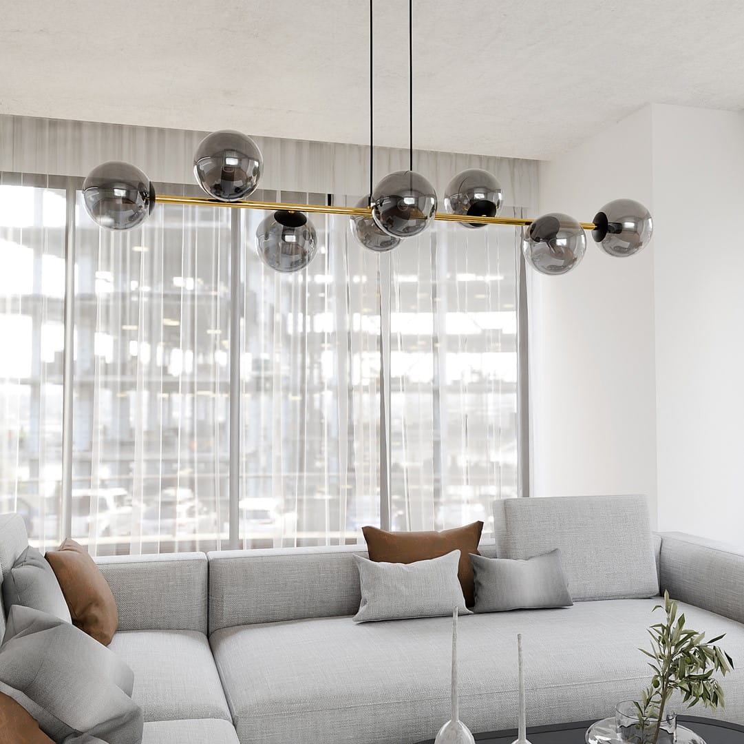 Lampa wisząca Gravity 8-punktowa w kolorze czarnym, złotym i grafitowym, z metalową konstrukcją oraz szklanymi kulami w odcieniu grafitowym. Zawieszona nad szarym narożnikiem, w jasnym wnętrzu z dużymi oknami i zasłonami.