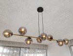 Lampa wisząca Gravity 8-punktowa w kolorze czarnym, złotym i grafitowym. Składa się z metalowego stelaża z ośmioma szklanymi kulami w odcieniu grafitowym, zawieszona na cienkich linkach. Ujęcie z dołu, ukazujące detal i konstrukcję lampy.