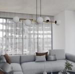 Lampa wisząca Gravity 6-punktowa w kolorze czarnym i złotym z opalowymi kloszami. Ułożona poziomo nad szaro-beżową sofą w jasnym wnętrzu z dużymi oknami i zasłonami. Klosze o okrągłym kształcie, z czarnymi detalami, zawieszone na cienkich linkach.