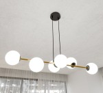 Lampa wisząca Gravity 6-punktowa z czarnym mocowaniem i złotą rurą, z sześcioma białymi, okrągłymi kloszami. Wisząca, w układzie poziomym, z długimi, czarnymi przewodami, w nowoczesnym wnętrzu z białymi firanami w tle.