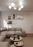 Lampa sufitowa Magnum 6-punktowa w kolorze białym i złotym, z sześcioma okrągłymi kloszami. Ujęcie z dołu, montowana na suficie. W tle widoczna aranżacja salonu z obrazami na ścianie oraz jasną sofą.