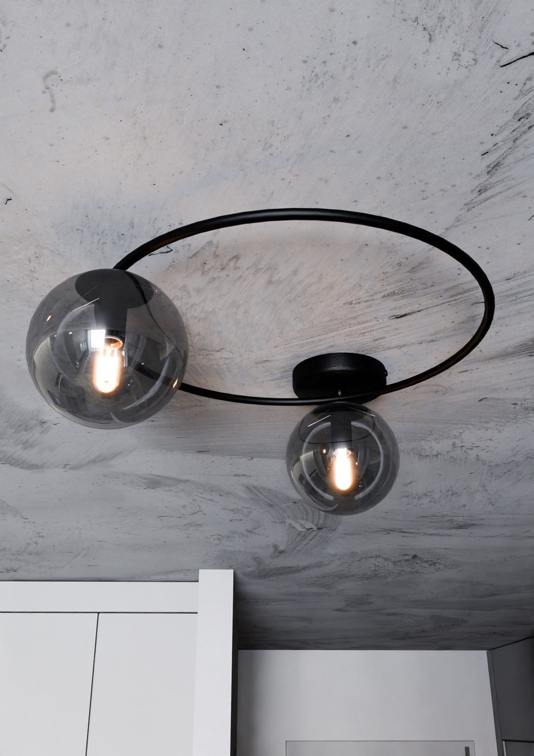 Lampa sufitowa Sopra 2-punktowa w kolorze czarnym i grafitowym, z dwoma szklanymi kloszami w kształcie kul, montowana na okrągłej podstawie. Widok z dołu, na gładkim, betonowym suficie.