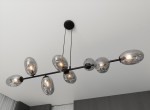 Lampa wisząca Pandora 8-punktowa w kolorze czarnym i grafitowym, z ośmioma szklanymi kloszami w kształcie owalnym. Umożliwia regulację wysokości, zawieszona na cienkich linkach z sufitu, idealna do nowoczesnych wnętrz.