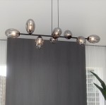Lampa wisząca Pandora 8-punktowa w kolorze czarnym i grafitowym, z ośmioma szklanymi kloszami w kształcie jajek. Ułożona na prostym metalowym stelażu, wisi pod kątem, tworząc nowoczesną aranżację w przestrzeni. Tło w odcieniach szarości.