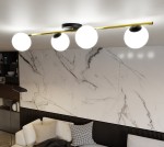 Lampa sufitowa Splendi 4-punktowa w kolorze czarnym i złotym z opalowymi kloszami. Ujęcie z góry, produkt zamontowany na suficie, z czterema okrągłymi, białymi kloszami na złotej rurze, na tle jasnej, marmurowej ściany.