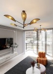 Lampa sufitowa Vene 6-punktowa w kolorze czarnym z rattanowymi kloszami, umieszczona na suficie w nowoczesnym wnętrzu. Klosze mają kształt liści, emitując ciepłe światło. W tle widoczny pokój dzienny z oknem i meblami.