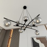 Lampa wisząca Essa 8-punktowa w kolorze czarnym i grafitowym, z sześcioma okrągłymi, przezroczystymi kloszami. Produkt zawieszony na cienkich linkach, z centralnym mocowaniem sufitowym. W tle widoczne minimalistyczne wnętrze z dekoracyjnymi panelami.