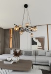 Lampa wisząca Essa, 8-punktowa, w kolorze czarnym z miodowymi kloszami, zawieszona na cienkich linkach. Ujęcie z dołu, ukazujące elegancki design z wieloma okrągłymi żarówkami. Tło to nowoczesne wnętrze z szarym narożnikiem i dekoracjami.