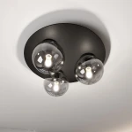 Trzypunkowa lampa sufitowa w kolorze czarnym z grafitowym stelażem. Okulary lamp wykonane z przezroczystego szkła, z widocznymi żarówkami w środku. Produkt zamontowany na okrągłej, matowej podstawie. Ujęcie z dołu, ukazujące całość lampy.