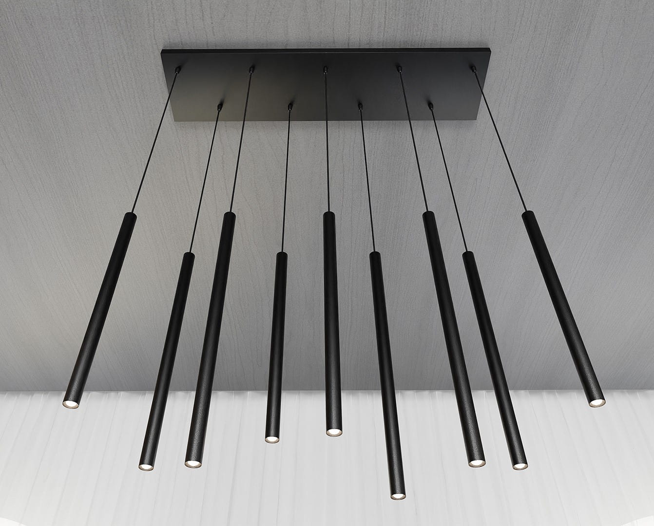 Lampa wisząca Selter 9-punktowa, czarna, z długimi, cylindrycznymi kloszami, zawieszona na cienkich linkach. Ujęcie z góry, ukazujące równomierne rozmieszczenie punktów świetlnych na prostokątnej podstawie. Tło w jasnym kolorze.