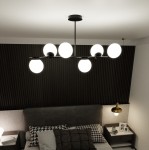 Lampa wisząca Bior 6-punktowa w kolorze czarnym, z sześcioma okrągłymi, białymi kloszami, zamontowana na prostym, metalowym stelażu. Widok z góry w nowoczesnej sypialni, na tle ciemnej, teksturowanej ściany.