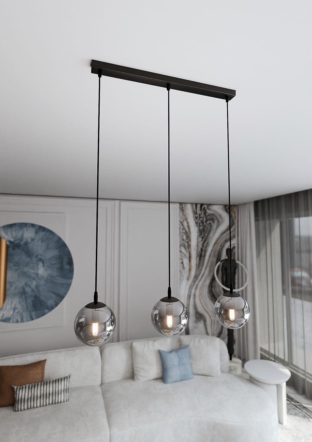 Lampa wisząca Cosmo 3-punktowa w kolorze grafitowym, z trzema okrągłymi kloszami w przezroczystym szkle. Ujęcie z góry, z zawieszeniem na cienkich linkach. Produkt umieszczony w nowoczesnym wnętrzu z kanapą w jasnych odcieniach.