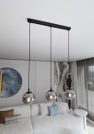 Lampa wisząca Cosmo 3-punktowa w kolorze grafitowym, z trzema okrągłymi kloszami w przezroczystym szkle. Ujęcie z góry, z zawieszeniem na cienkich linkach. Produkt umieszczony w nowoczesnym wnętrzu z kanapą w jasnych odcieniach.