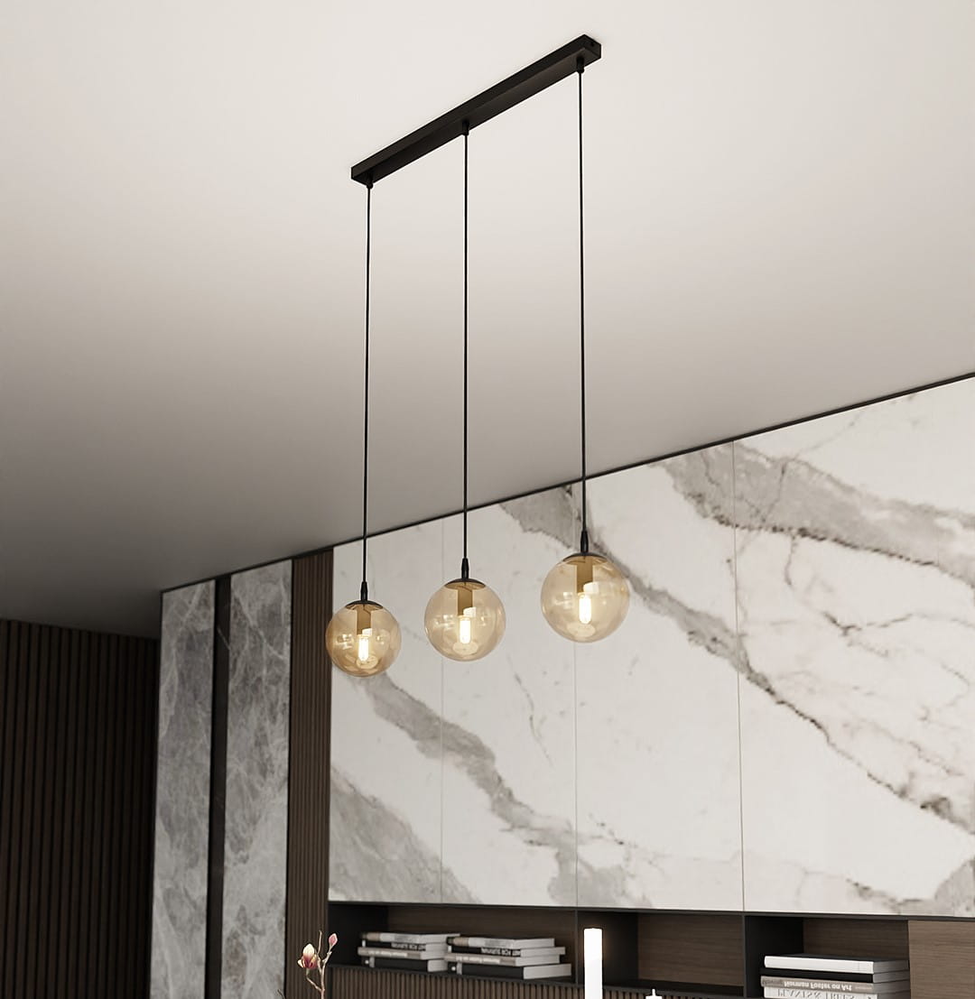 Lampa wisząca Cosmo 3-punktowa w kolorze miodowym, z trzema okrągłymi kloszami na czarnych przewodach. Montowana pod sufitem, z widocznym eleganckim wykończeniem oraz nowoczesnym tłem w odcieniach szarości z marmurowym wzorem.