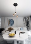 Lampa wisząca Cosmo Premium 3-punktowa w kolorze miodowym z trzema okrągłymi kloszami zawieszona na długich czarnych przewodach. Ujęcie z dołu, ukazujące lampę w nowoczesnym wnętrzu z jasną sofą i dekoracjami na stole.