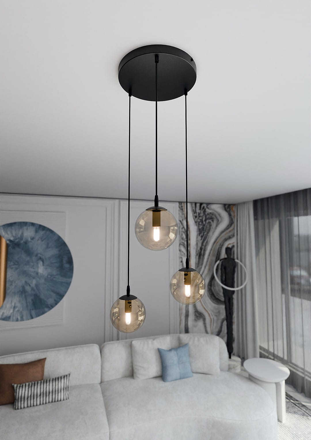 Lampa wisząca Cosmo Premium 3-punktowa w kolorze miodowym z trzema okrągłymi kloszami na czarnych przewodach. Klosze mają przezroczyste, teksturowane wykończenie. Produkt zawieszony na okrągłej, czarnej podstawie, we wnętrzu z jasną sofą i dekoracjami.