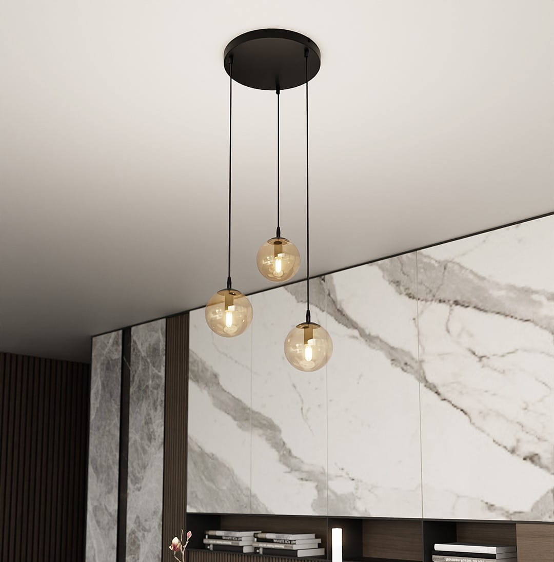 Lampa wisząca Cosmo Premium 3-punktowa w kolorze miodowym z trzema szklanymi kulami zawieszonymi na czarnych linkach, montowana na okrągłej podsufitce. Tło w odcieniach białych i szarych, z marmurowym wzorem.