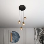 Czarna lampa wisząca Cosmo Premium z czterema szklanymi kloszami w miodowym odcieniu, zawieszona na długich linkach. Produkt umieszczony w nowoczesnym wnętrzu, z białym sufitem i dekoracyjną ścianą w tle.